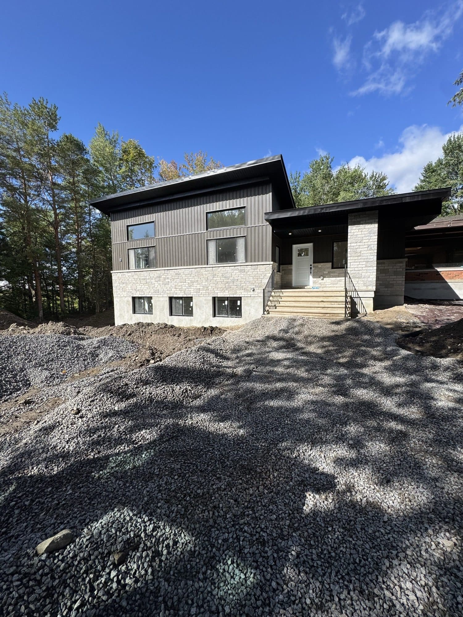 Two-storey modern exterior in grey board-and-batten and stone, with gravel still out front